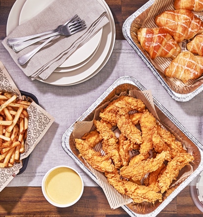 Delivery trays filled with Cheddar's fries, coleslaw, queso, chicken tenders, and honey butter croissants.