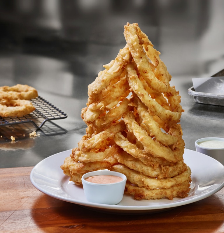 Tower of Cheddar's famous Homemade Onion Rings, served with a side of sauce.