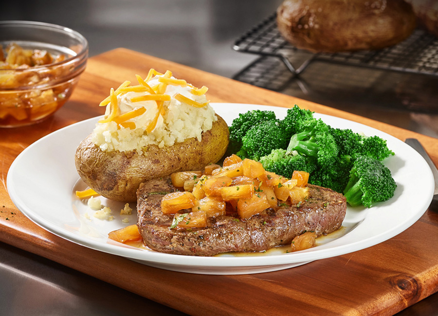 Cheddar's delicious center-cut top sirloin grilled with pineapple and a sweet Hawaiian glaze, served with broccoli and a loaded baked potato on a plate.